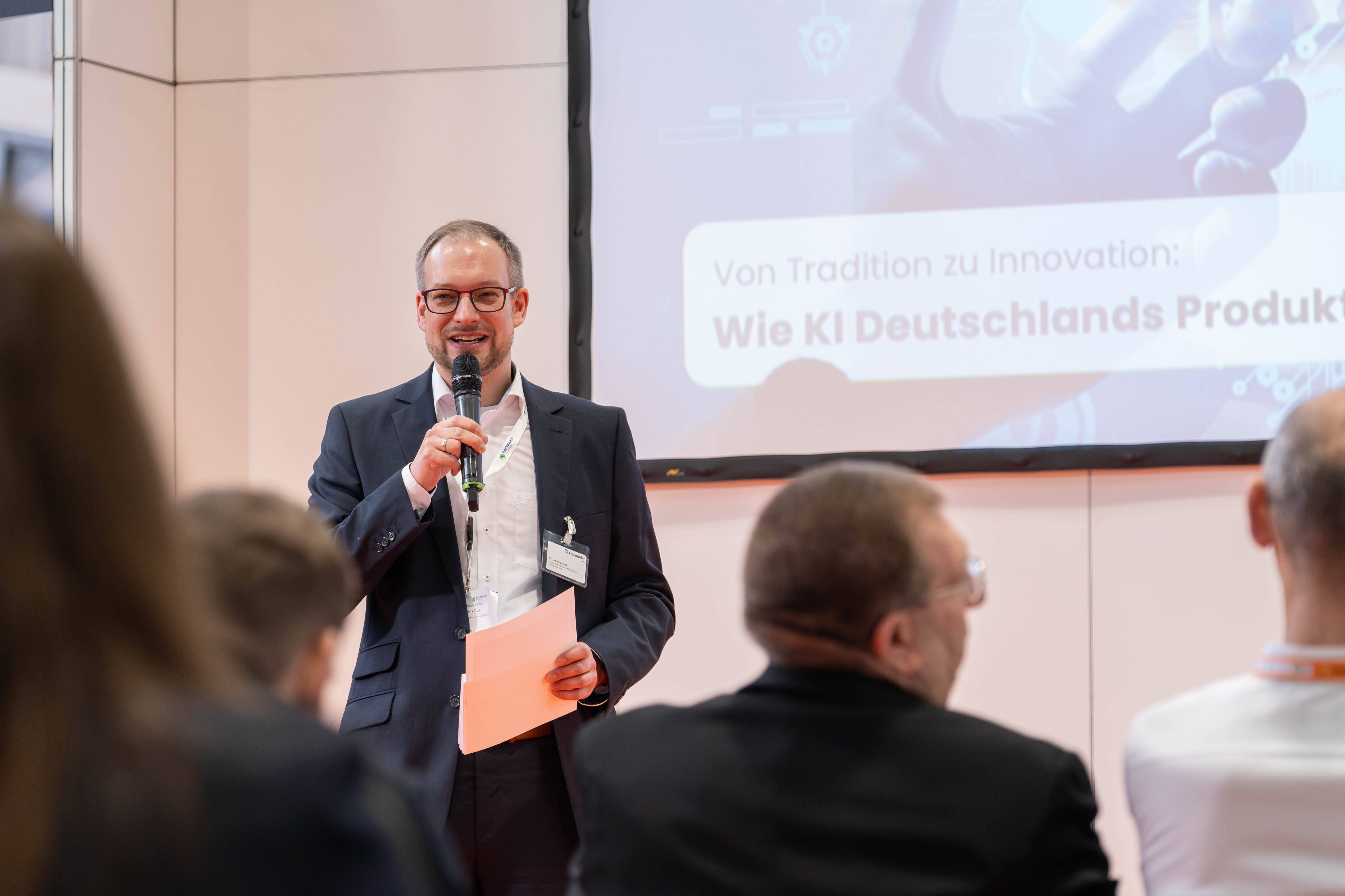 Ein Mann steht vor einem Publikum und spricht auf der maintenance Messe ins Mikrofon. Die maintenance in Dortmund ist die führende Fachveranstaltung zum Thema industrielle Instandhaltung und eine etablierte Bühne für Innovationen und Trends.. Der Mann moderiert das Vortragsforum ScienceCenter.